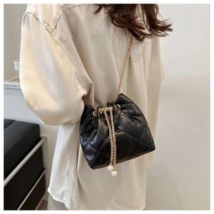 Detail of black quilted bucket bag featuring gold chain strap and decorative pearls