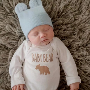 Dettaglio cappello neonato blu in maglia con pompon e body bianco con orsetto