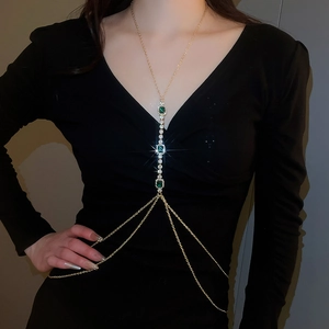 Detail of layered gold body chain with green crystals and rhinestones on a black dress