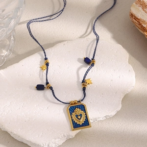 Detail of blue cord necklace with 18K gold-plated sacred heart pendant on white stone