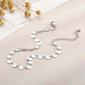 Silver stainless steel anklet with heart-shaped links on a soft beige background