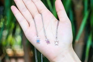 Detail of hand-held micro-pave zircon girl pendants in blue, pink, and white crystal