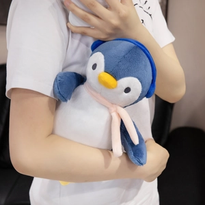 Close-up of cute penguin plush toy with pink scarf and blue earmuffs being held