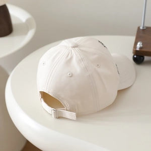 Detail view of beige cotton baseball cap featuring metal buckle and twill fabric texture