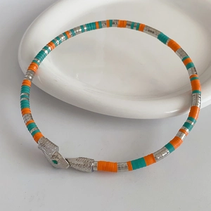 Macro detail of a silver snake bracelet with colorful stripes and green gemstone eyes