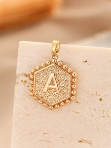 Close-up of golden hexagonal pendant with embossed letter A and hammered metal texture