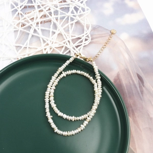 Double-layered natural pearl necklace with golden lobster clasp on a vintage green plate