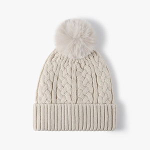 Creamy white cable knit beanie for women with a fluffy faux fur pom and ribbed cuff