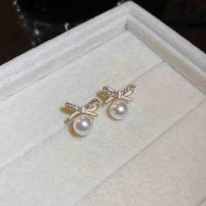 Vue macro de boucles d'oreilles nœud doré avec perles blanches et zircons brillants