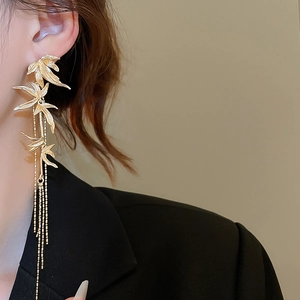 Close-up of elegant gold bamboo leaf tassel earrings worn by a model in a refined setting