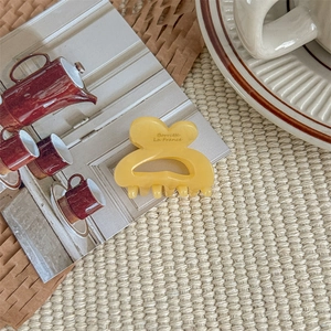Close-up of a small yellow translucent hair claw clip on a woven mat with vintage decor