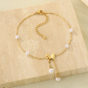 Golden butterfly anklet with white pearls on a textured stone, stylish summer accessory