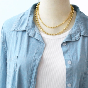 Close-up of layered gold ball chain necklace on a model with denim shirt