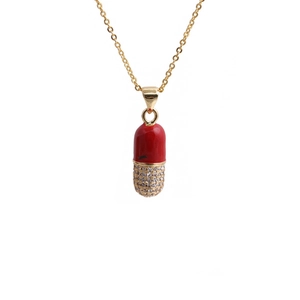 Gold chain necklace with red enamel and zircon pill pendant on white background