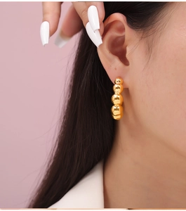Close-up of a model wearing tiered golden bead drop earrings with a polished finish