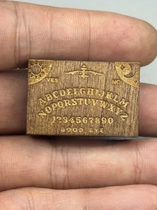 Macro detail of miniature wooden spirit board featuring engraved alphabet and sun moon motifs