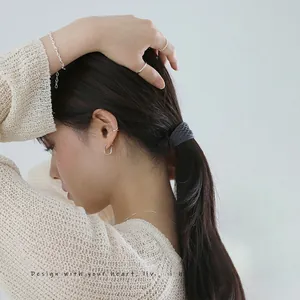 Close-up of minimalist dark grey braided hair scrunchie worn with silver jewelry set