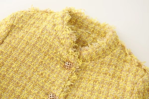 Macro detail of yellow tweed jacket showing gold buttons and frayed collar texture