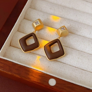 Close-up of diamond-shaped brown earrings with gold frame in a velvet jewelry box