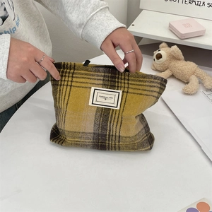 Detail of yellow plaid canvas makeup bag featuring Pleasant Time woven label on white desk