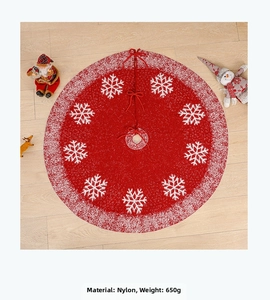 Detail of red knit Christmas tree skirt with white snowflake patterns on wooden floor