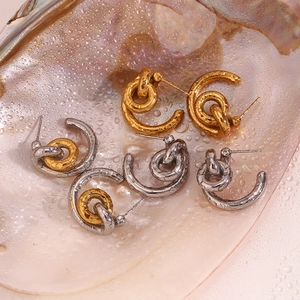Macro detail of textured 18K gold and silver hoop earrings on a wet seashell surface