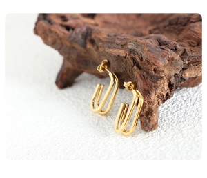 Close-up of golden U-shaped geometric stud earrings on a textured wood and fabric background