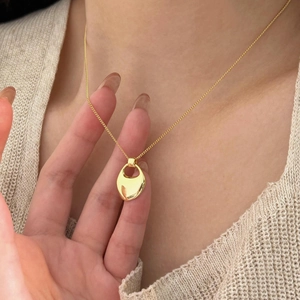 Close-up of minimalist gold oval pendant necklace worn over beige knitwear
