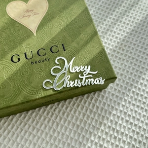 Close-up of green embossed Gucci Beauty gift box with Merry Christmas cake topper ornament
