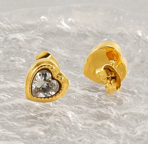 Close-up of gold heart stud earrings with clear zircon on water ripple glass