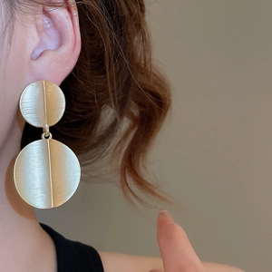 Close-up of matte gold geometric round drop earrings with brushed metal texture on a model