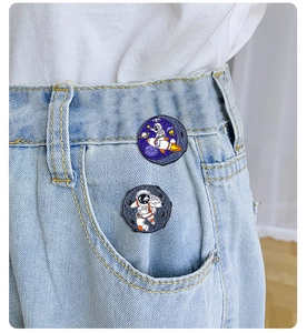 Detail of astronaut and rocket enamel pins on denim pocket with vibrant star patterns