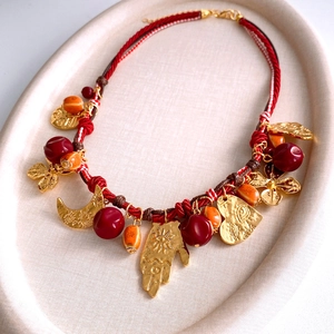 Dettaglio collana bohémien in corda rossa con cuore in resina e ciondoli vintage in metallo