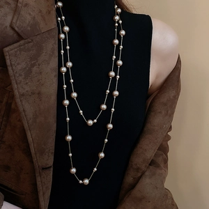Detail of double-layer champagne pearl long necklace worn over a black turtleneck