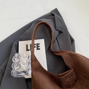 Close-up of a large brown suede hobo tote bag styled with a grey blazer and book