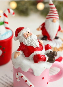 Detail of a resin Santa Claus lying on a pink mug with festive decor and warm lights