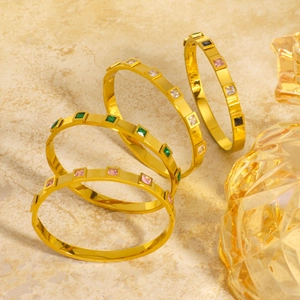 Goldene Titanstahl-Armbänder mit quadratischen Zirkonia auf einer Marmorfläche