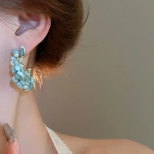 Detail view of model wearing gold-plated hoop earrings with blue aquamarine beads