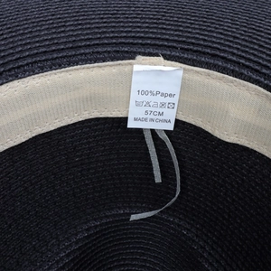 Detail of a 57cm black woven straw hat showing the 100% paper material label inside