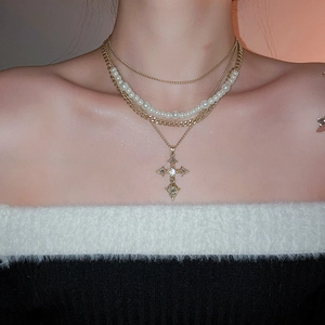 Close-up of layered gold necklace with pearl strands and sparkling crystal cross pendant
