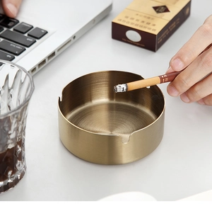 Brushed gold stainless steel ashtray on a modern desk with office stationery