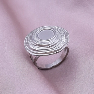 Detail of silver geometric oval ring with concentric relief texture on a pink silk background