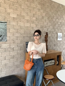 Detail view of woven orange bucket bag paired with a white textured short sleeve shirt