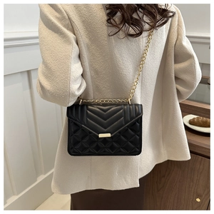 Detail of black quilted chain bag on model showing size and styling on a beige outfit
