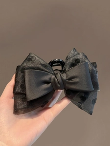 Detail of a large black polka dot organza and satin bow hair claw clip held in hand