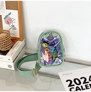 Close-up of mint green PVC transparent crossbody bag with metal buckles on glass surface