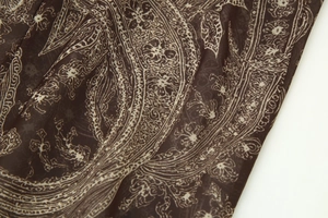 Gros plan du motif paisley sur tissu mousseline marron montrant la texture textile