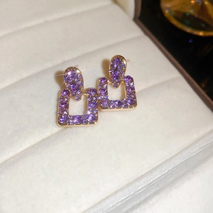 Dettaglio di orecchini quadrati placcati oro con strass viola su espositore bianco