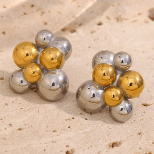 Vue macro de boucles d'oreilles bicolores or et argent sur un support en pierre beige