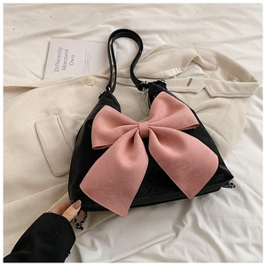 Detail of black shoulder bag featuring a large pink bow on white bedding and trench coat